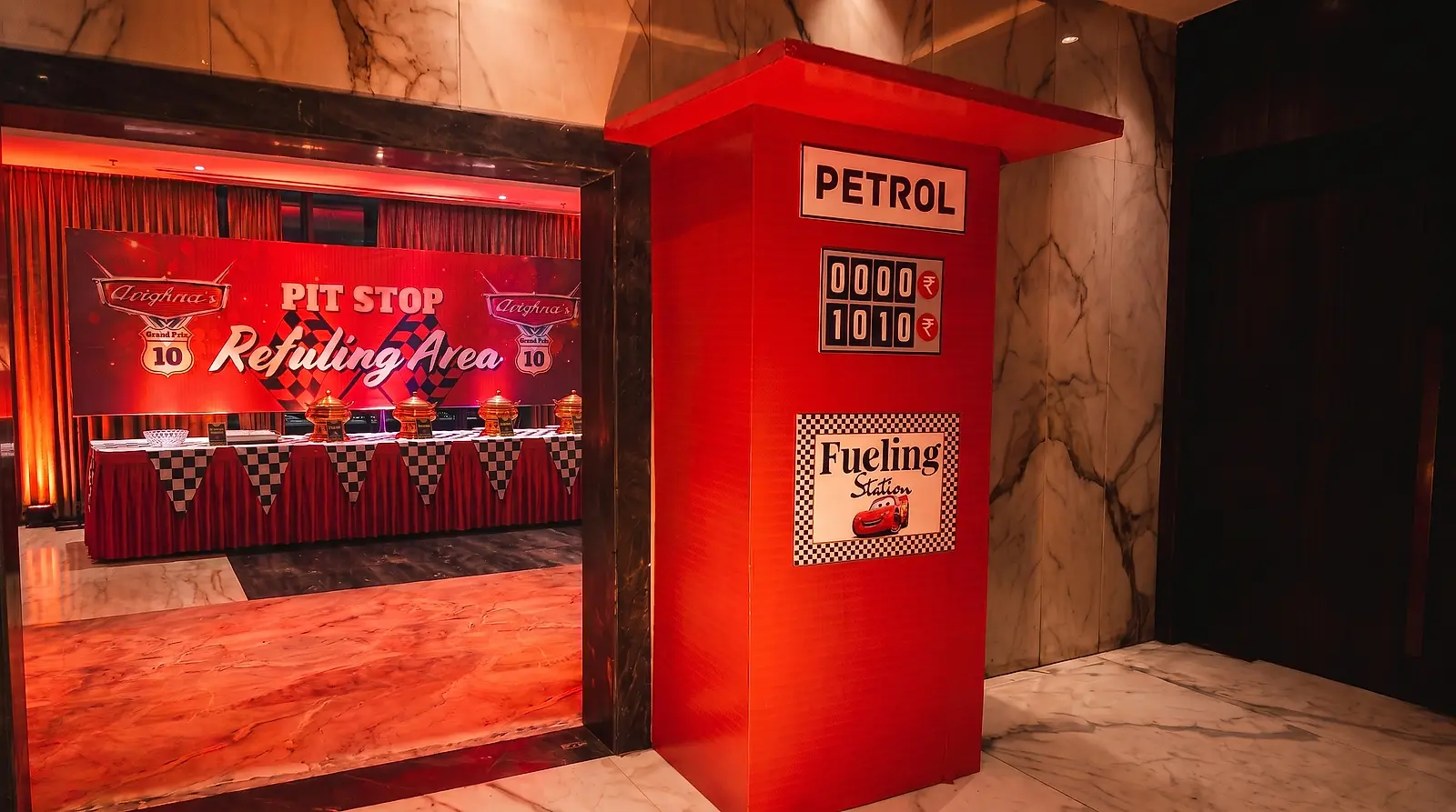 Custom-built red petrol pump prop with a fuelling station sign standing beside the catering area at a 10th birthday in Lake Town, Kolkata