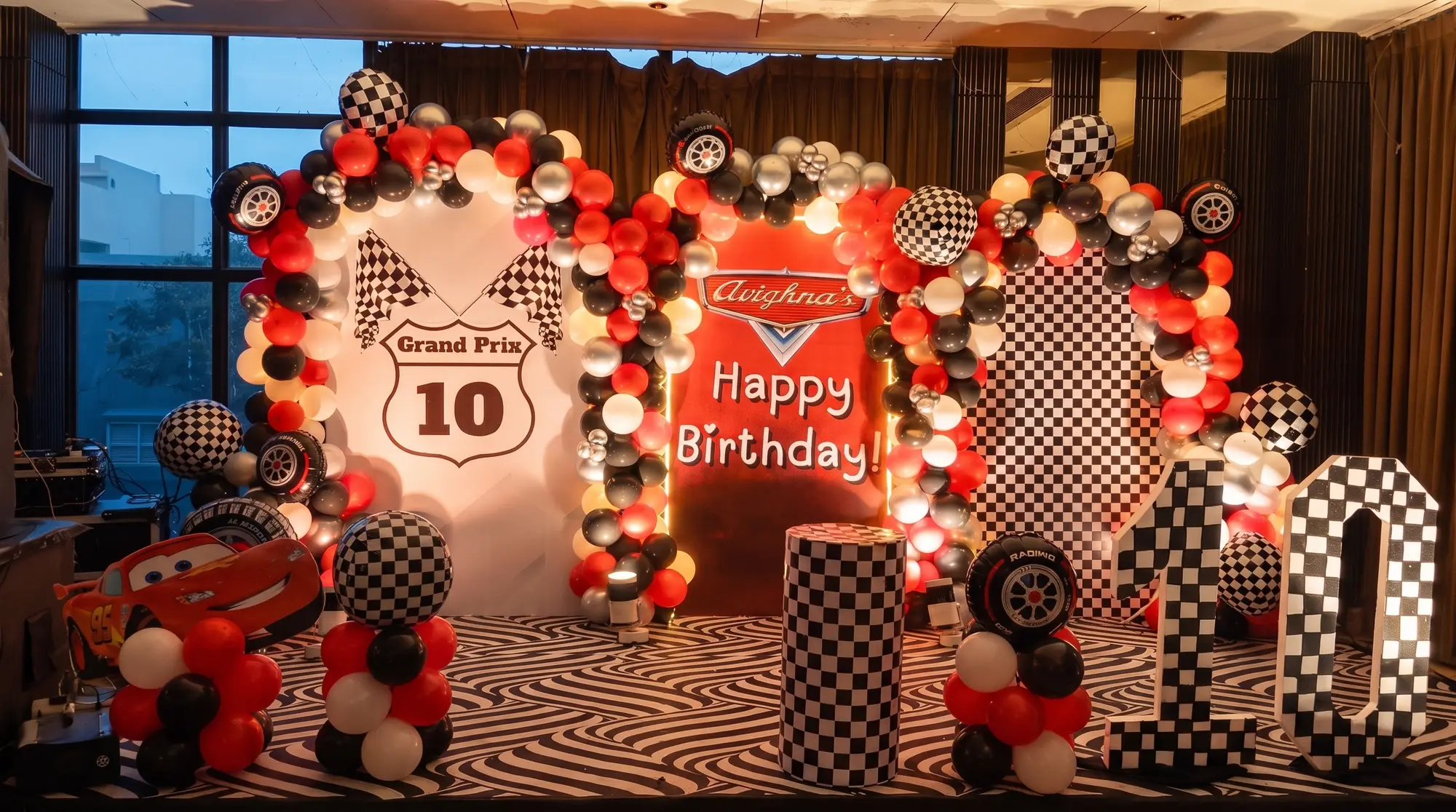 Birthday stage backdrop reading Grand Prix 10 with chequered flags, tyre balloons and giant chequerboard numerals at a 10th birthday in Lake Town, Kolkata