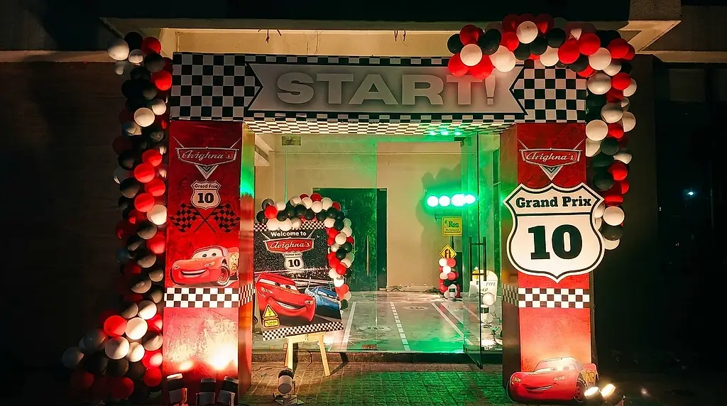 Race-themed entrance arch reading START, with chequered flag panels, red black and white balloon columns and a welcome standee at a 10th birthday in Lake Town, Kolkata
