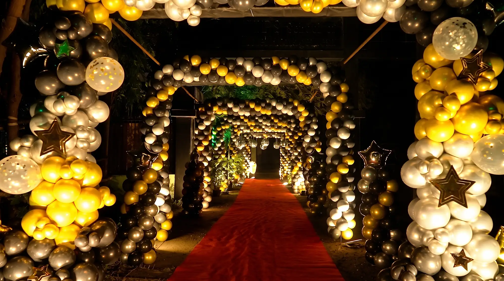 Red carpet running through successive gold, silver and black balloon archways with foil stars at the entrance to a 40th birthday at Elysian Lawn, Salt Lake, Kolkata